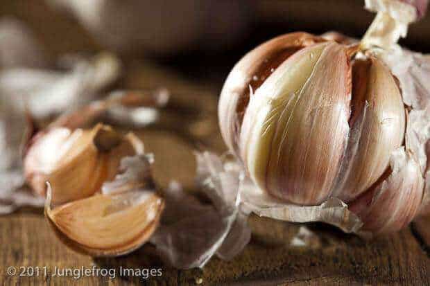 A ball of garlic with some cloves lying next to it on wood