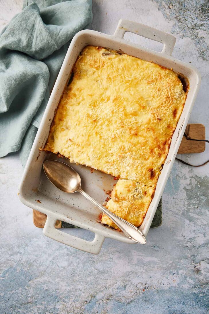 Finished moussaka dish placed on a wooden board on a table with a napkin