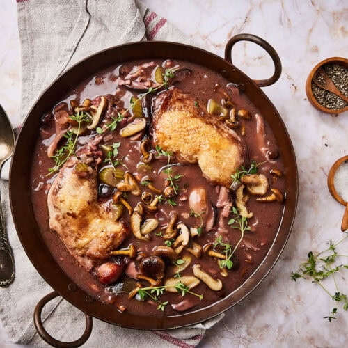 Easy coq au vin recipe in a pan with herbs and a spoon