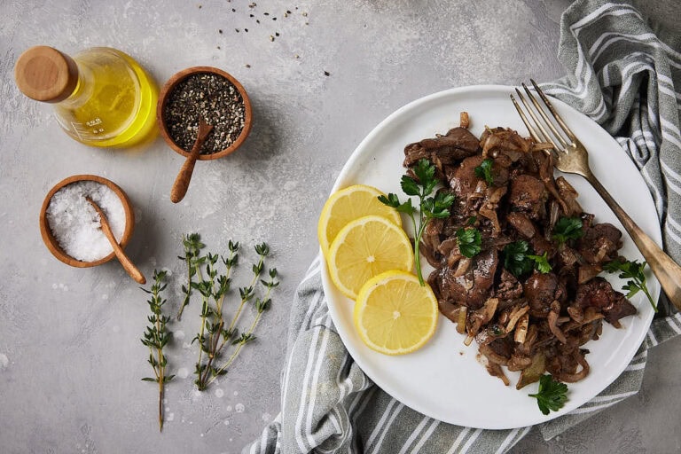 Plate with prepared chicken liver on a grey background with herbs