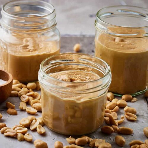 Peanut butter recipe in three jars with some peanuts around it