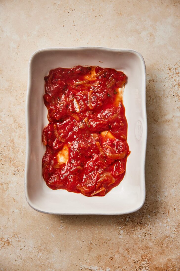 Making layers for the eggplant parmigiana. Start by adding a small layer of tomato sauce to the oven dish