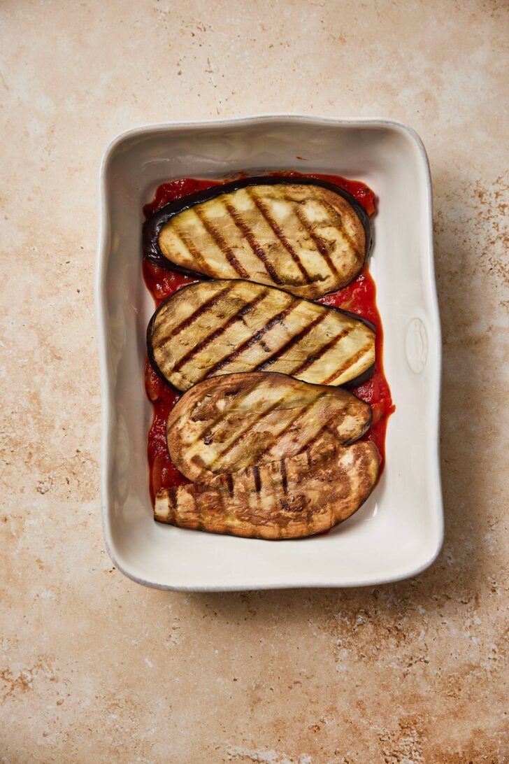 Adding the eggplant. Laying out the layers of eggplant on top of the tomato sauce